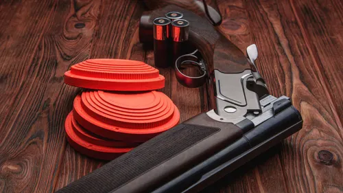 Shotgun resting beside a stack of orange clay targets